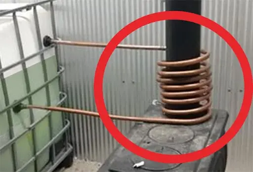 Copper heating coil on a wood stove pipe for free hot running water, from No Grid Survival Projects