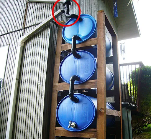 Stacked blue barrel rainwater harvesting system fed by a downspout, from No Grid Survival Projects